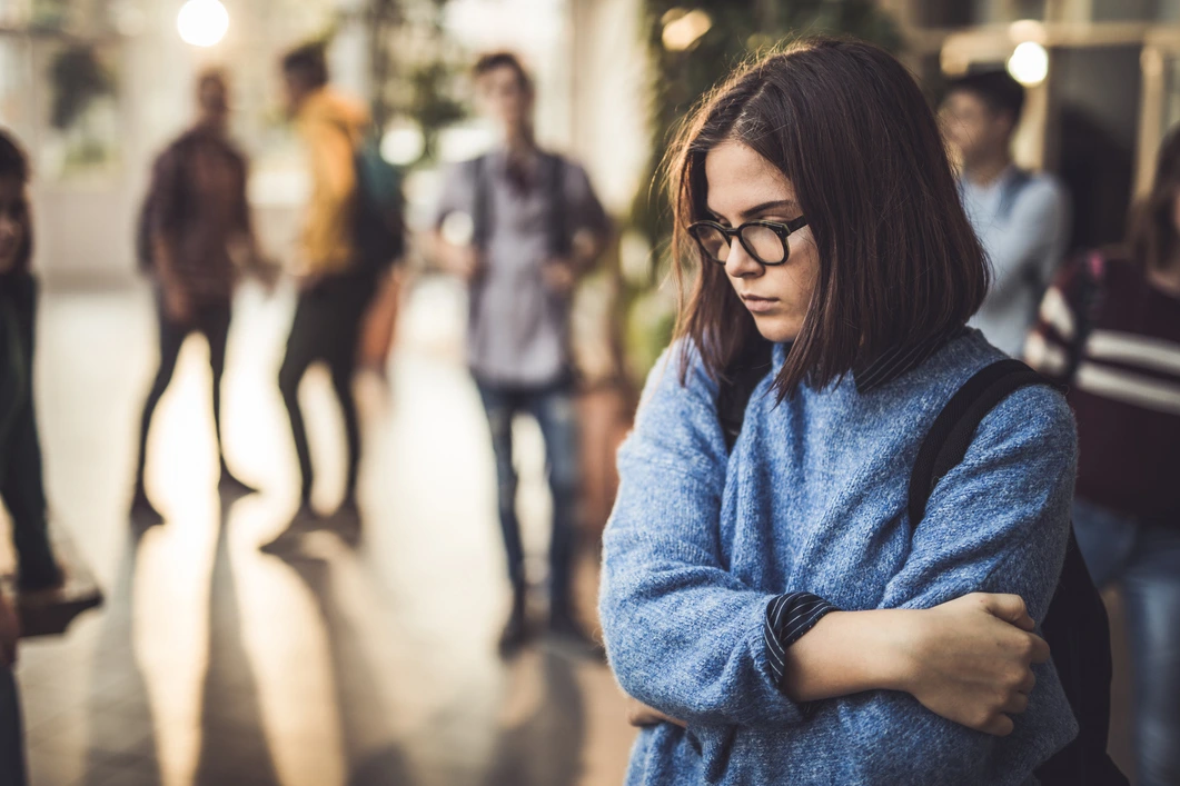 Anxious girl in the foreground with socializing teens in the background